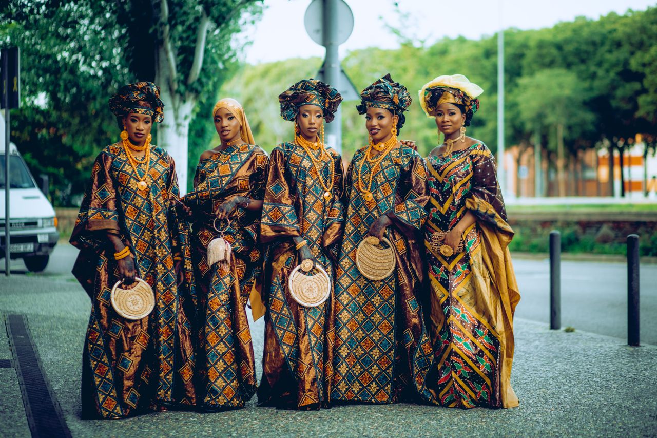 Group of African women in vibrant traditional clothing posing outdoors, showcasing cultural fashion.
